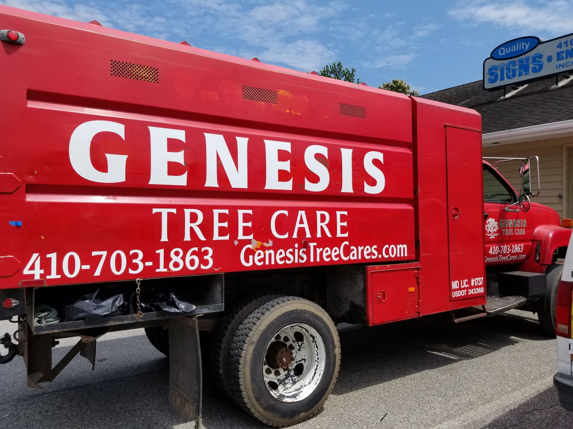 A red genesis tree care truck is parked on the side of the road