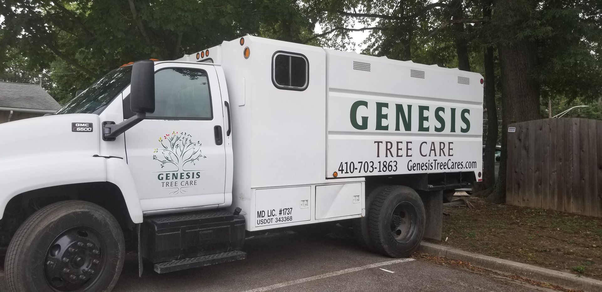 A white genesis tree care truck is parked in a parking lot