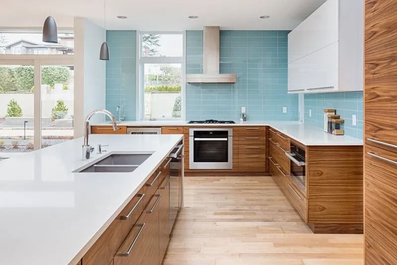 Modern kitchen with light wood cabinets, white countertops, and teal tile backsplash.