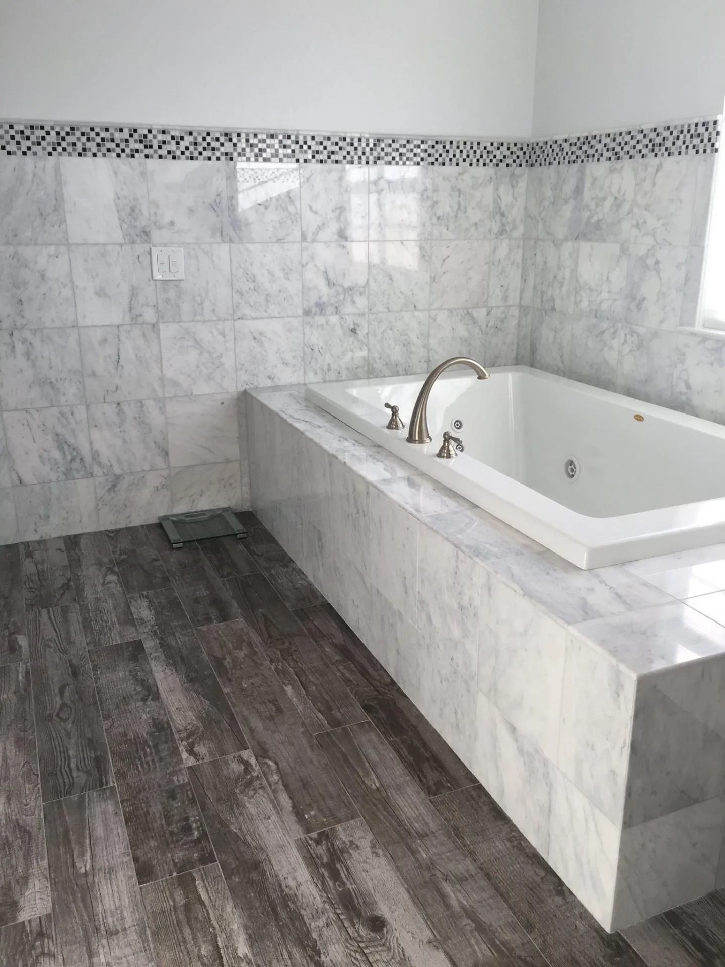 Bathroom with marble tile walls and tub surround, white tub, and wood-look flooring.