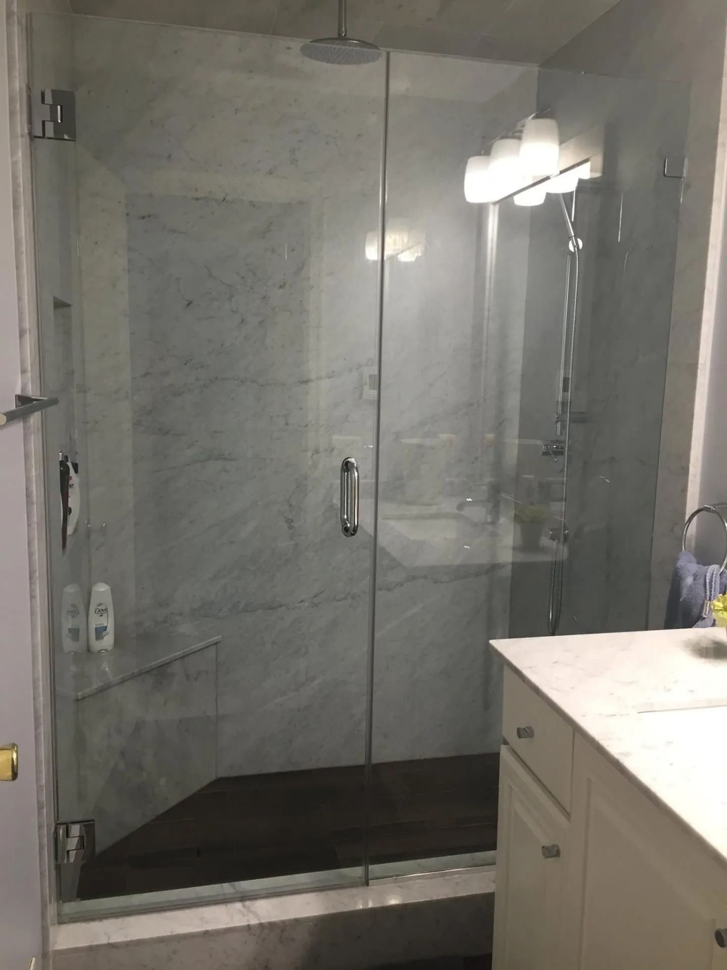 Glass shower with marble walls and a white vanity.