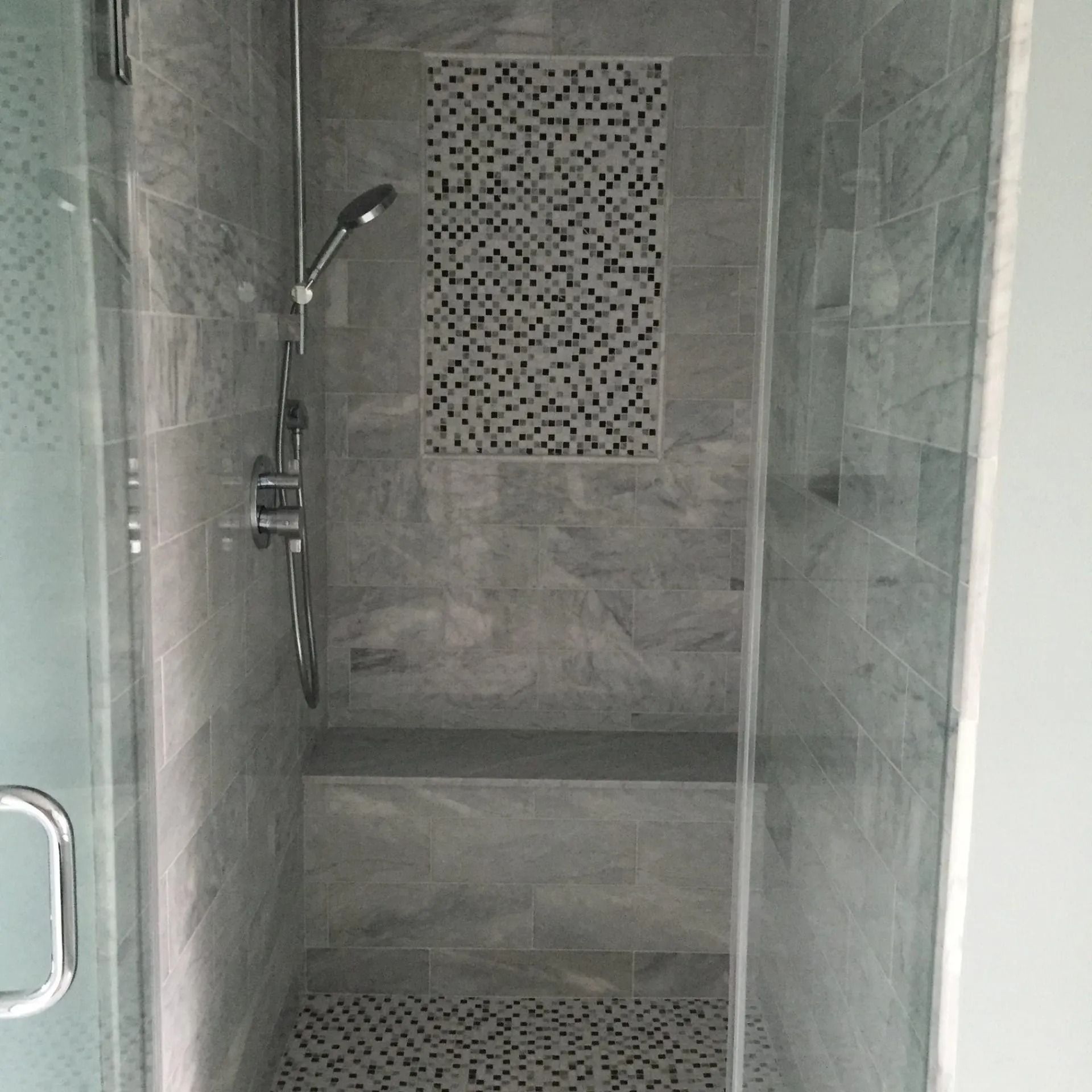 Gray-tiled shower with a pebble floor and mosaic accent. A built-in bench sits at the bottom.