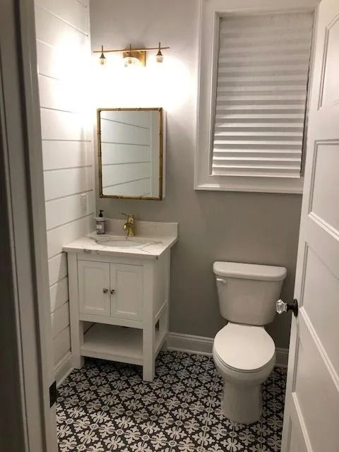 Small, renovated bathroom with shiplap walls, patterned floor tiles, white vanity, and toilet.