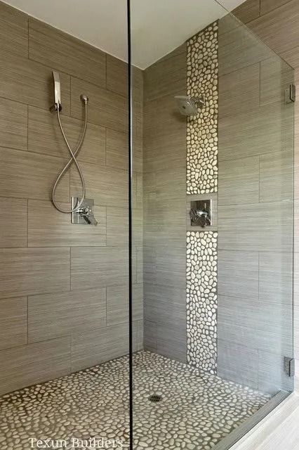 Shower with gray tiled walls and pebble-stone floor. Glass door. One showerhead. Stone accent strip.