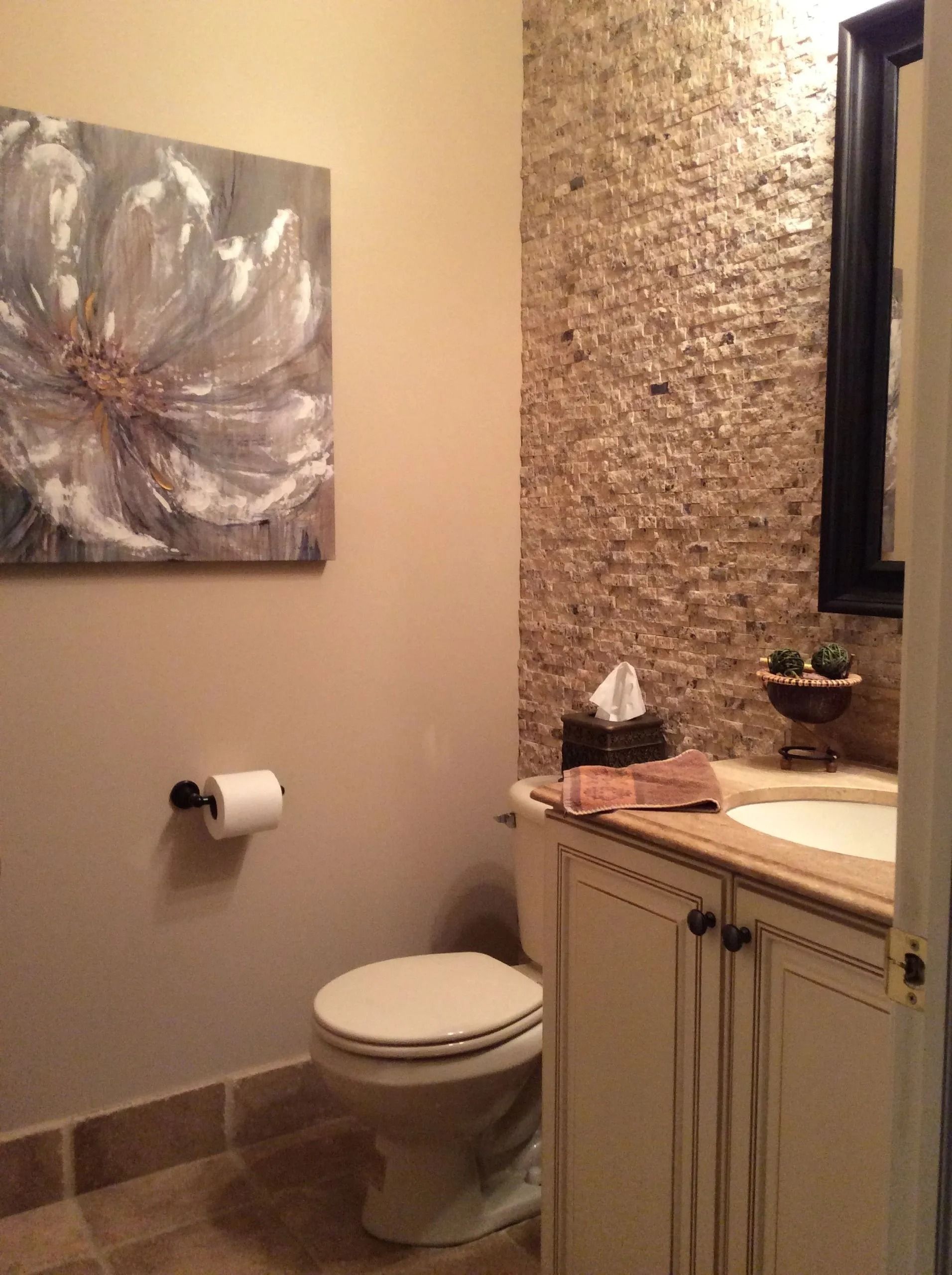 Small bathroom with stone accent wall, toilet, sink, and floral artwork.