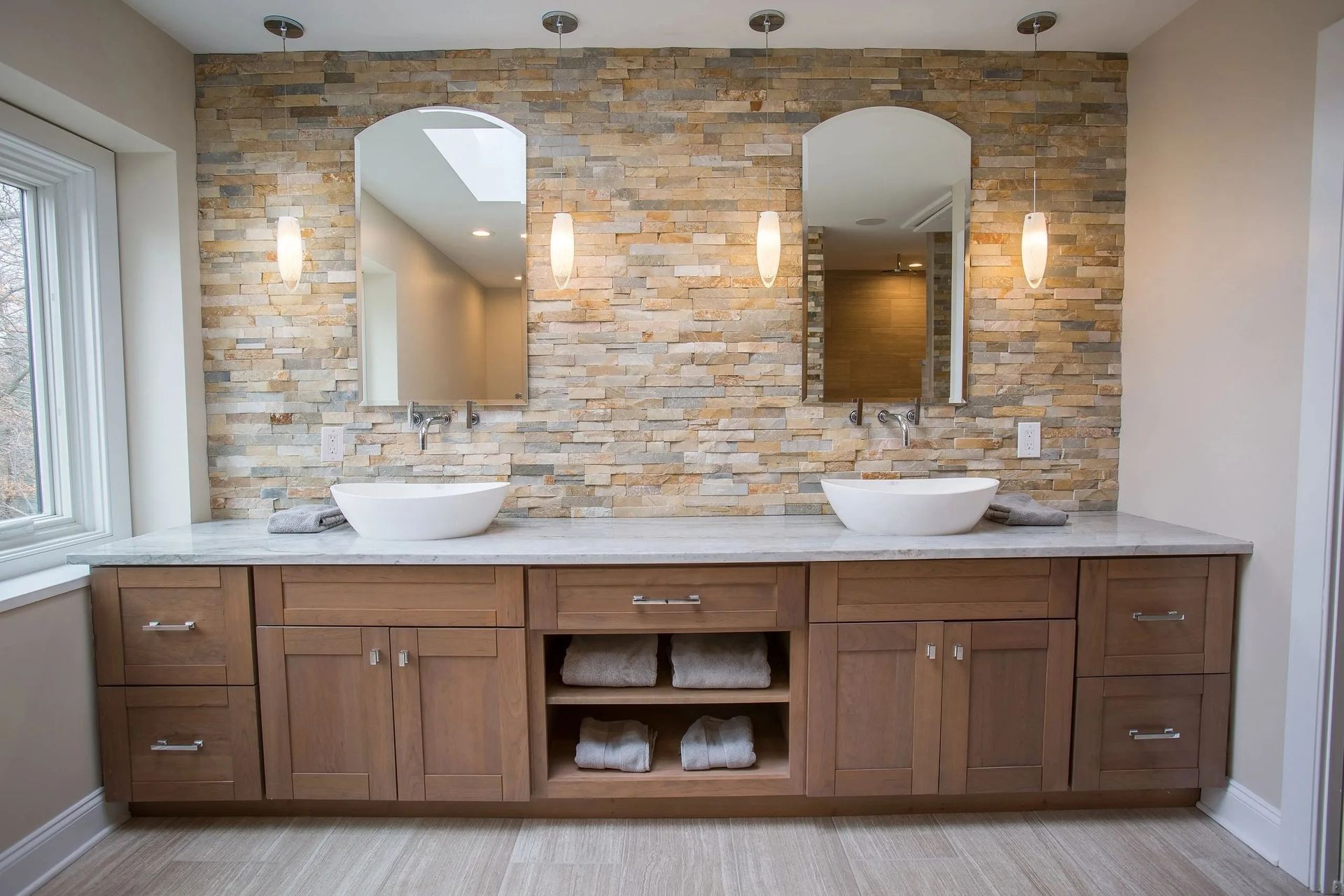 Bathroom with stone wall, two mirrors, vessel sinks, and wooden vanity.