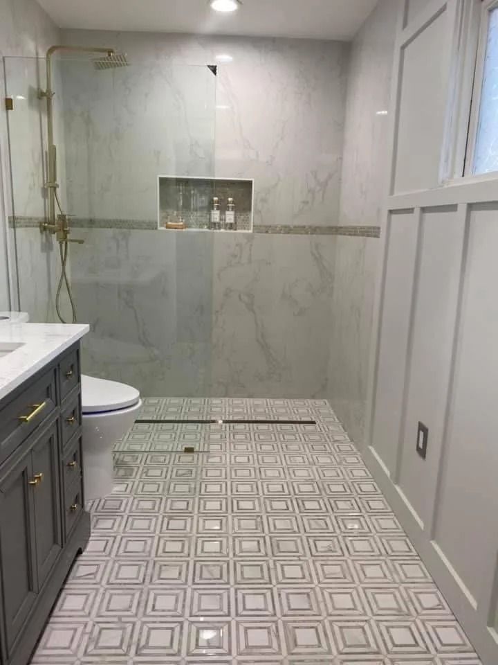 Bathroom with marble tile floor and walls, gray vanity, and gold shower fixtures.
