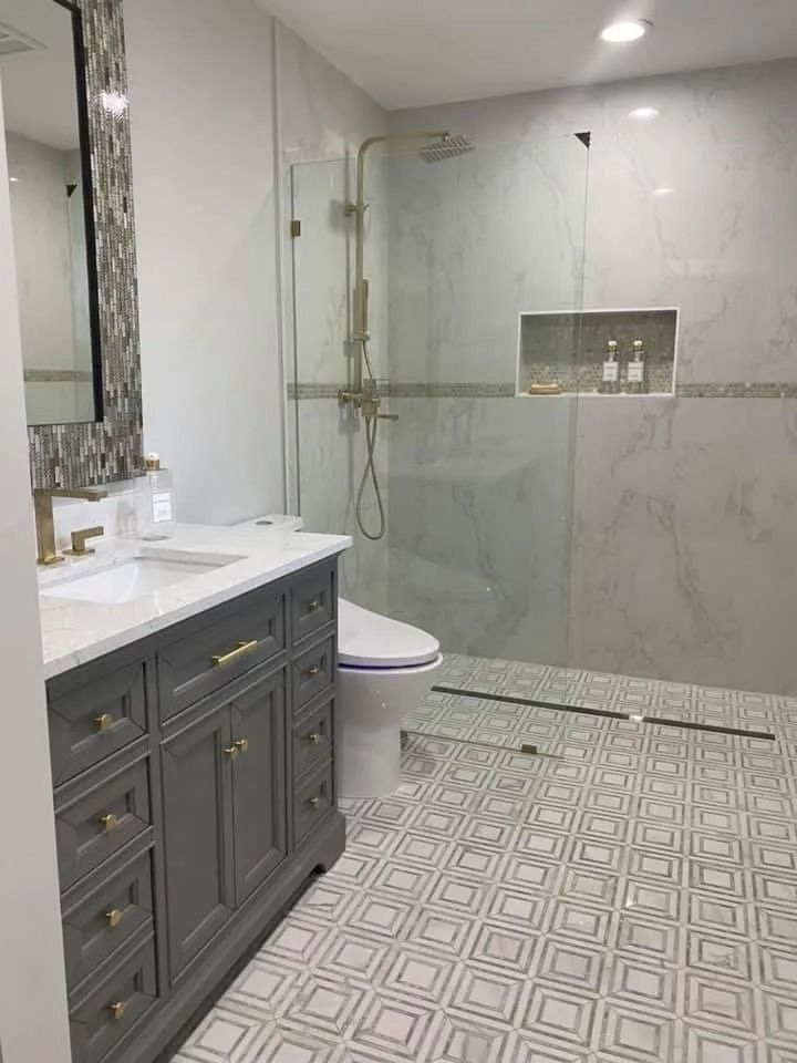 Gray and white bathroom with a shower, vanity, and toilet; gold fixtures and patterned tile.