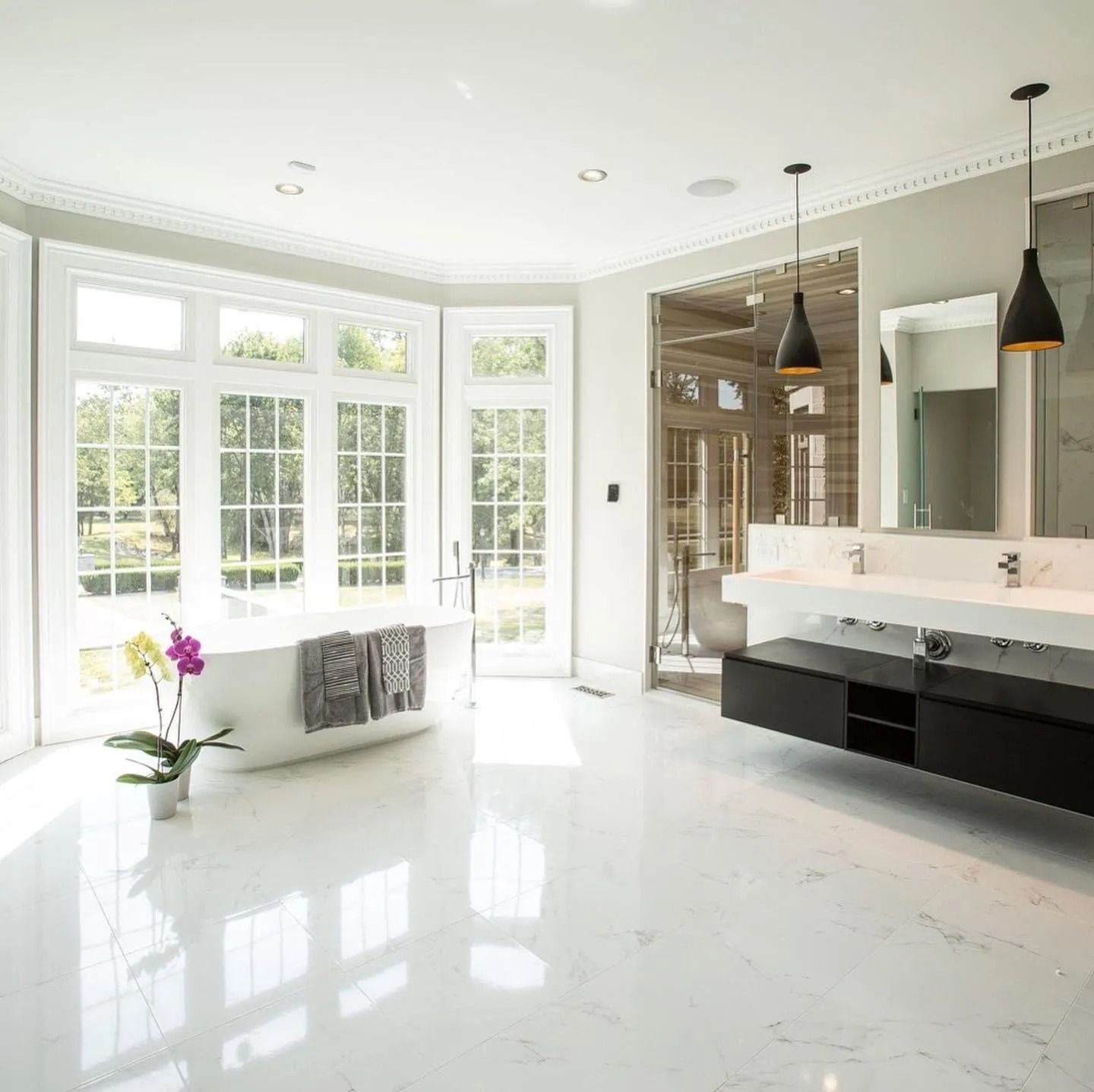Bright, modern bathroom with large windows, freestanding tub, double vanity, and black pendant lights.