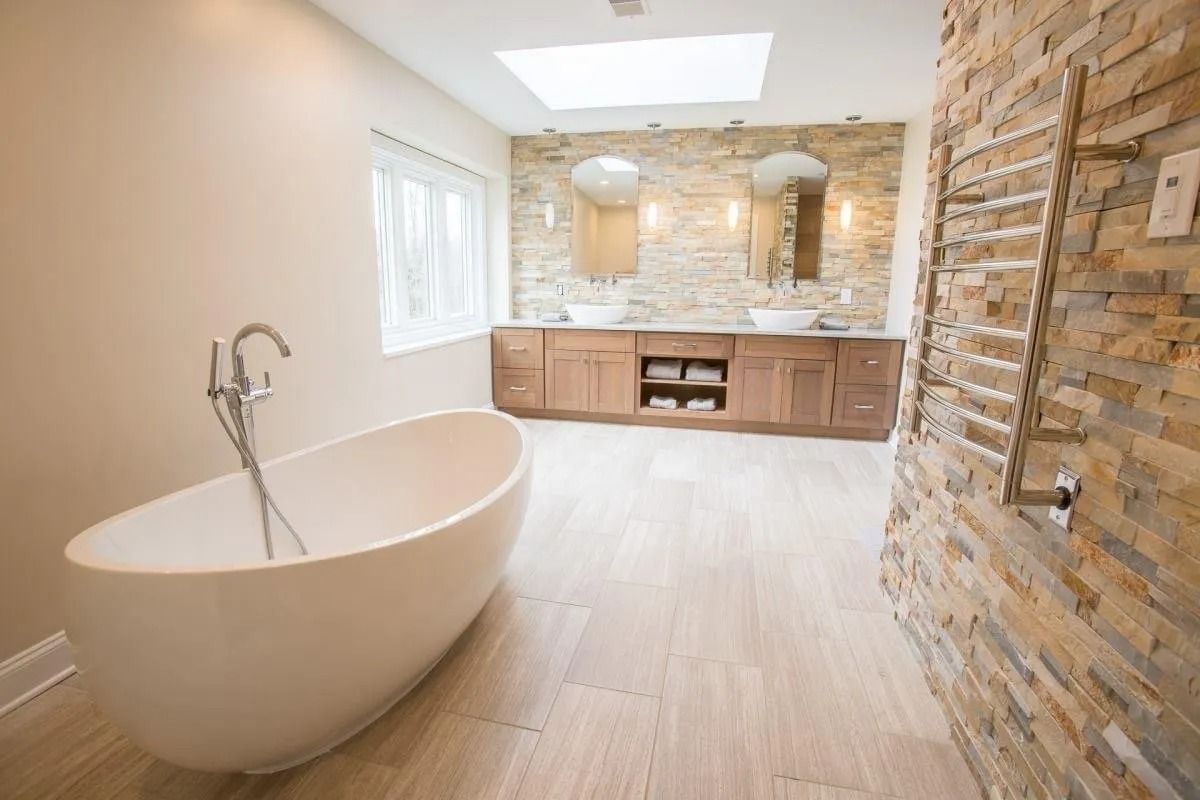 Modern bathroom with a freestanding tub, wood vanity, and stone accent wall.