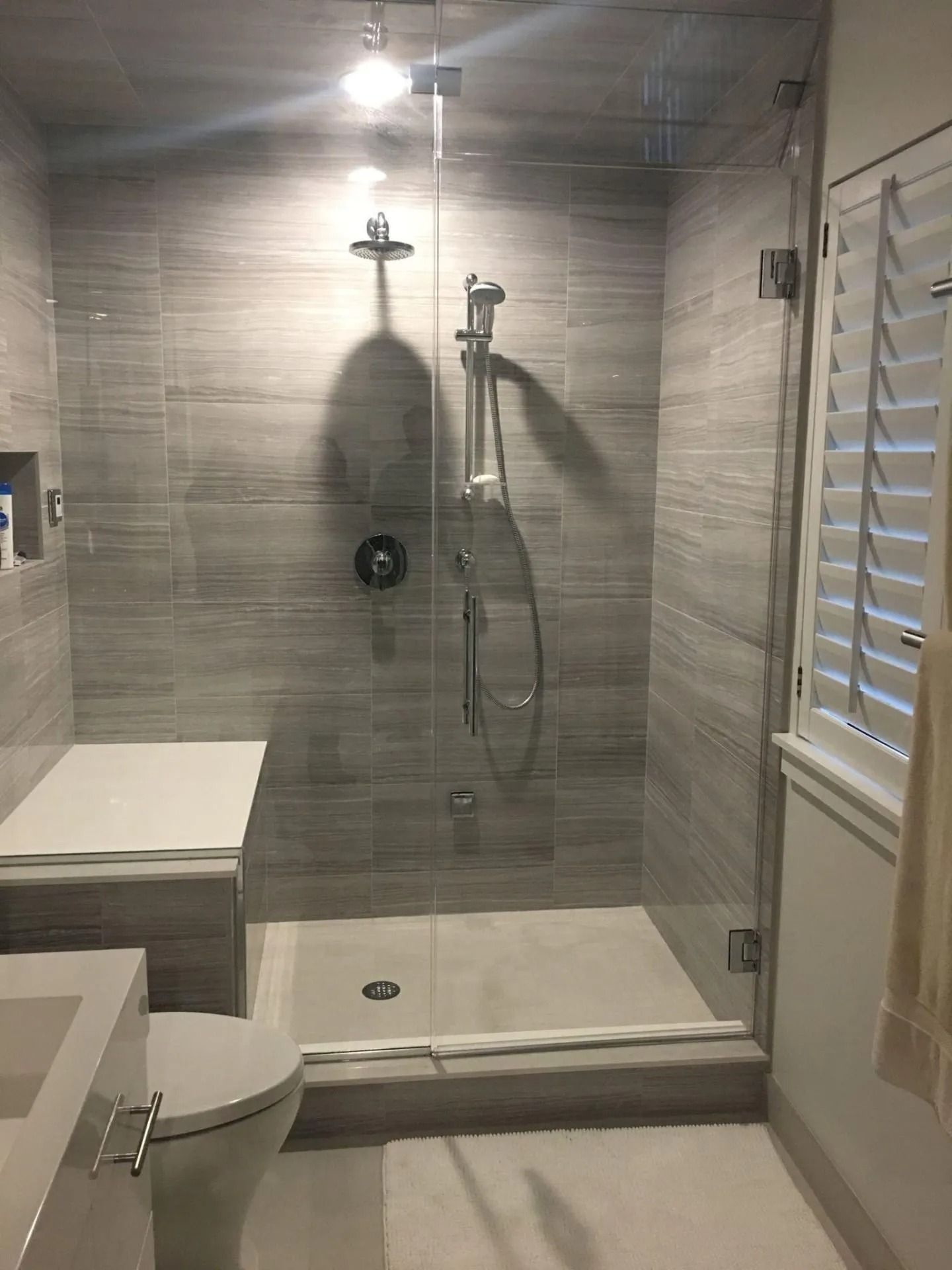 Modern gray tile shower with glass doors, built-in bench, and rain showerhead.