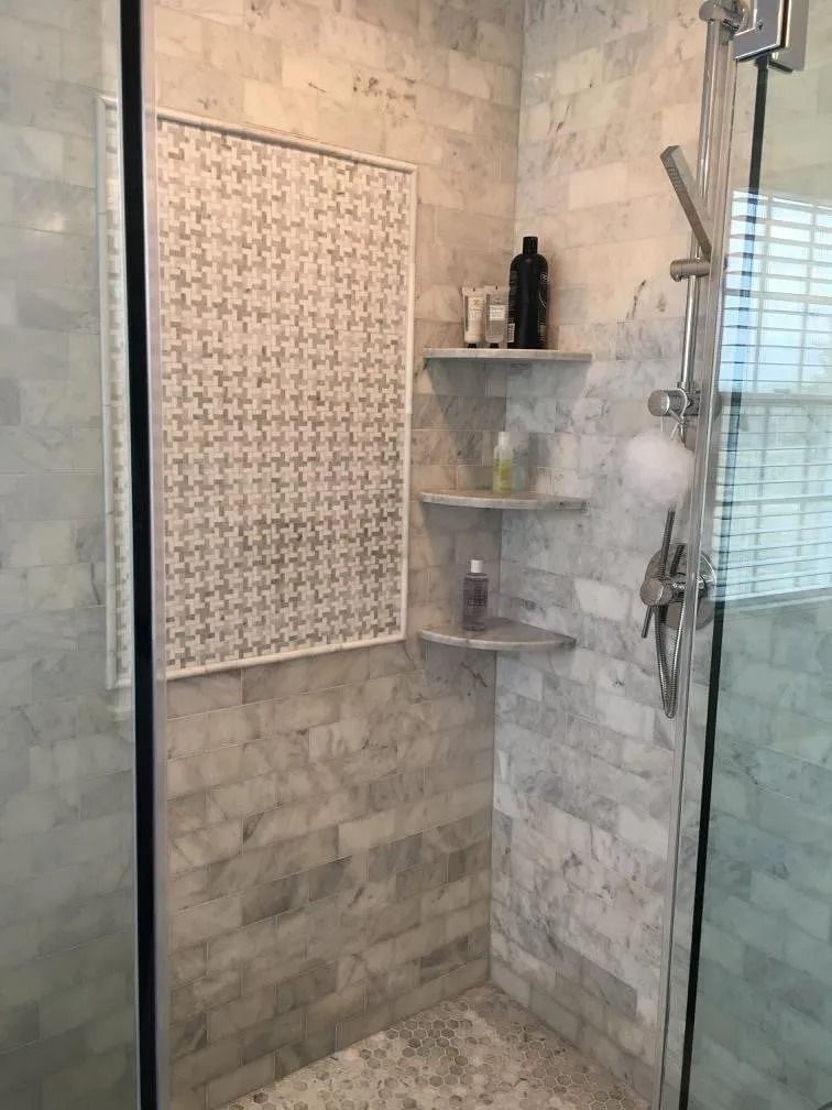 Marble tiled shower with shelves and decorative accent.