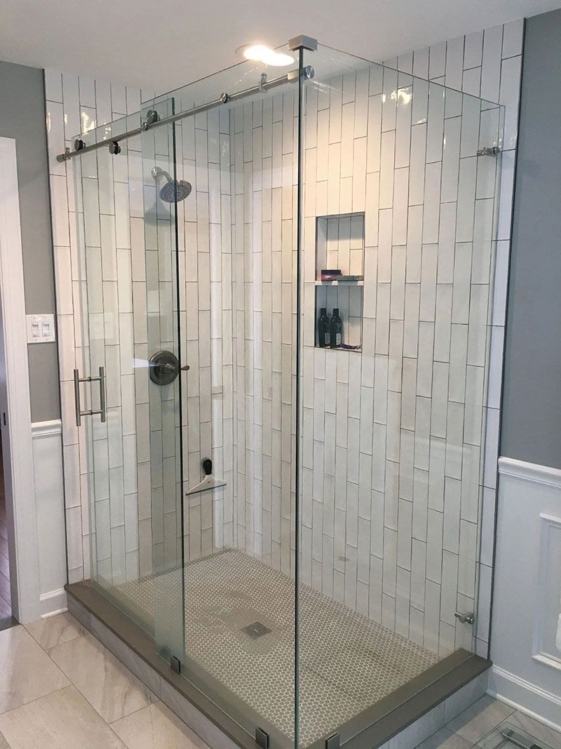 Glass-enclosed shower with white textured tile walls, a dark grey border, and a built-in shelf.