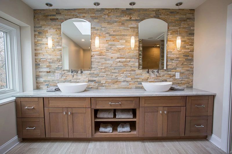 Bathroom with a stone accent wall, dual mirrors, and a wooden vanity with sinks.