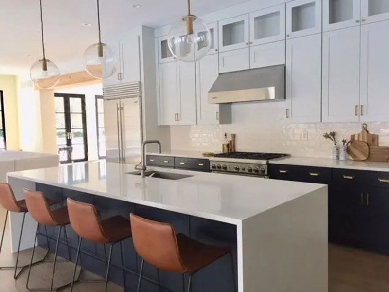 Modern kitchen with white and navy cabinets, large island with brown bar stools, and globe pendant lights.