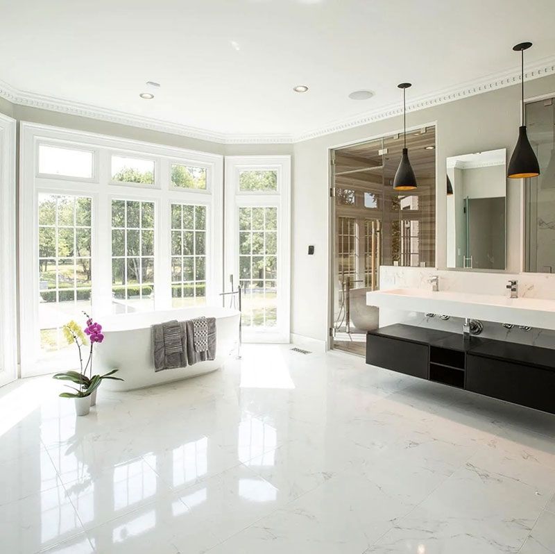 Bright, modern bathroom with large windows, freestanding tub, black floating vanity, and pendant lights.