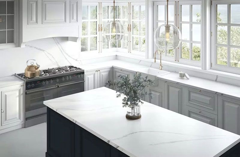 Elegant white kitchen with marble countertops, island, and large windows.