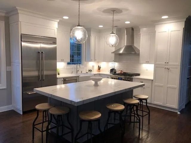 Modern white kitchen with stainless steel appliances, marble island, and pendant lights.