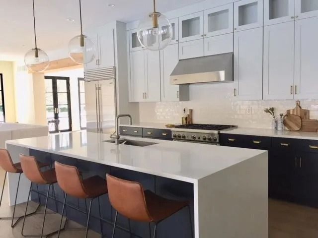 Modern kitchen with white countertops, navy island, and leather bar stools.