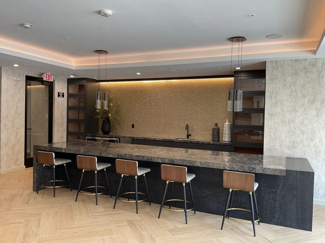 Modern bar area with seating, granite countertop, and gold tiled backsplash.