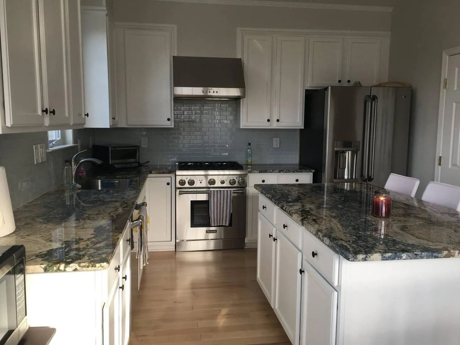 White kitchen with granite countertops, stainless steel appliances, and island with seating.