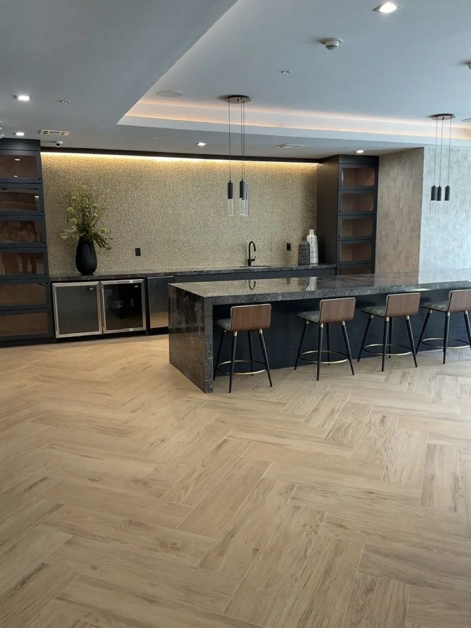 Modern kitchen with an island and bar stools, light wood floors, and decorative backsplashes.