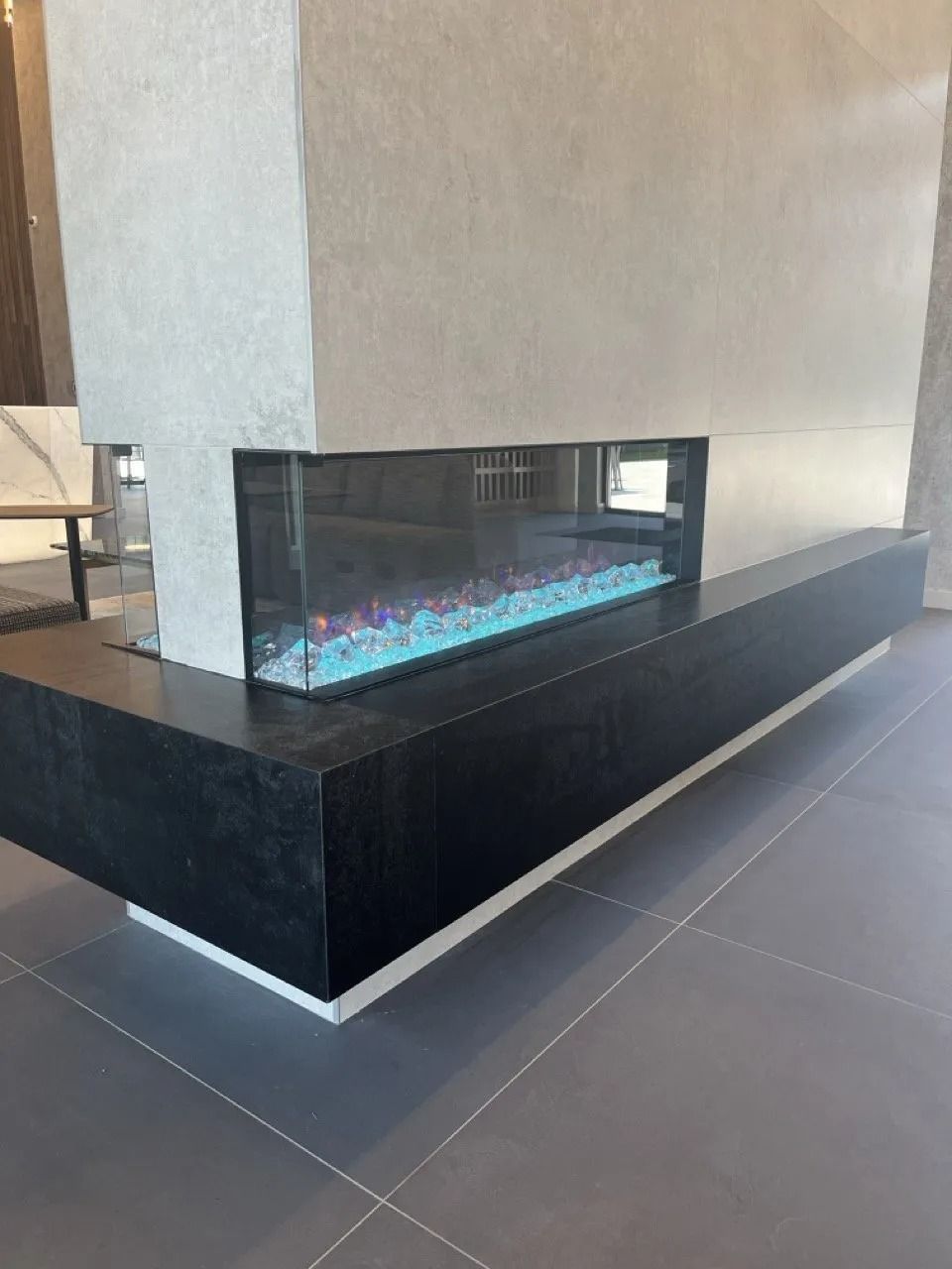 Modern, corner fireplace with a black base and gray concrete surround. Blue and purple flames are visible.