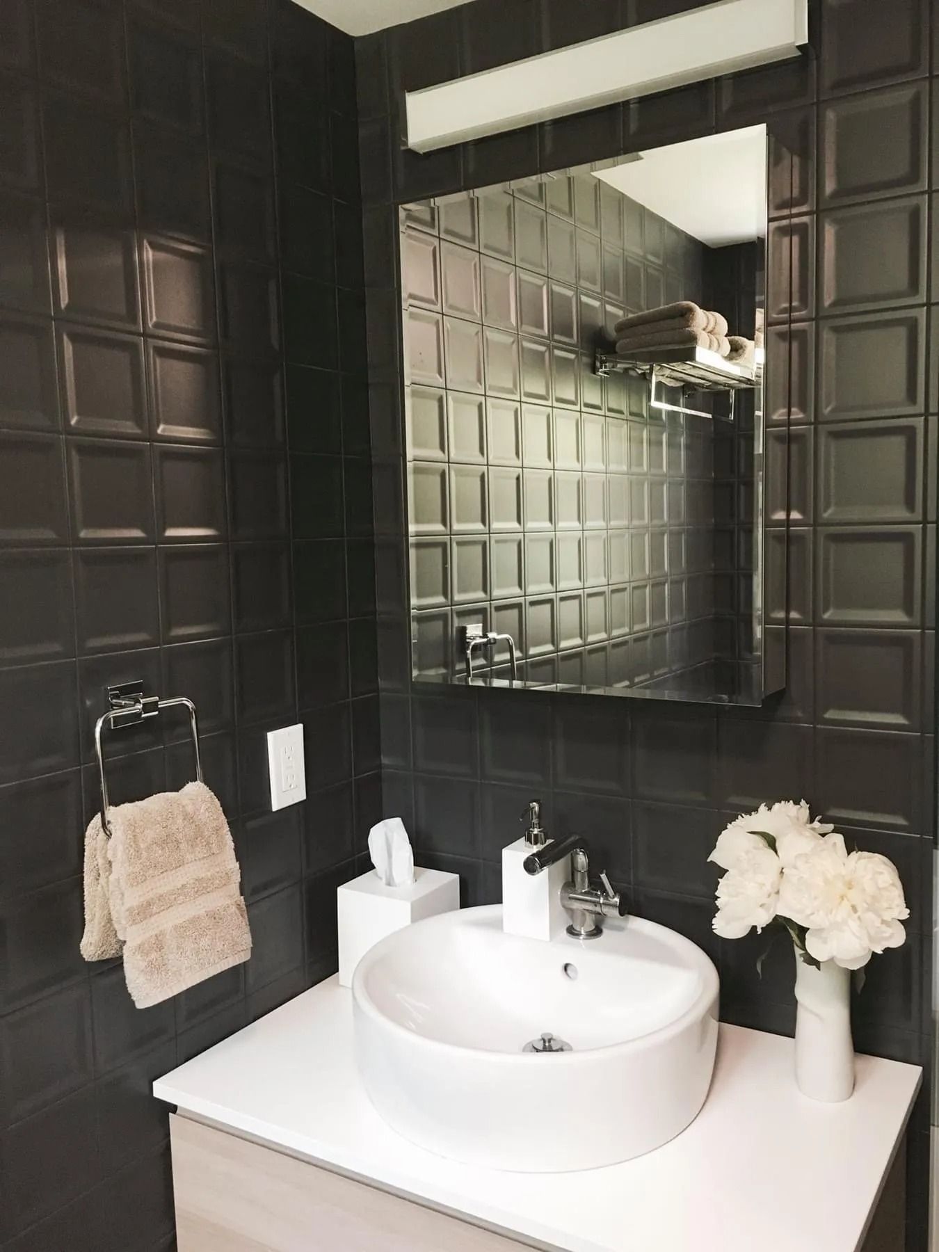 Small modern bathroom with black textured tile walls, white sink, and mirror.
