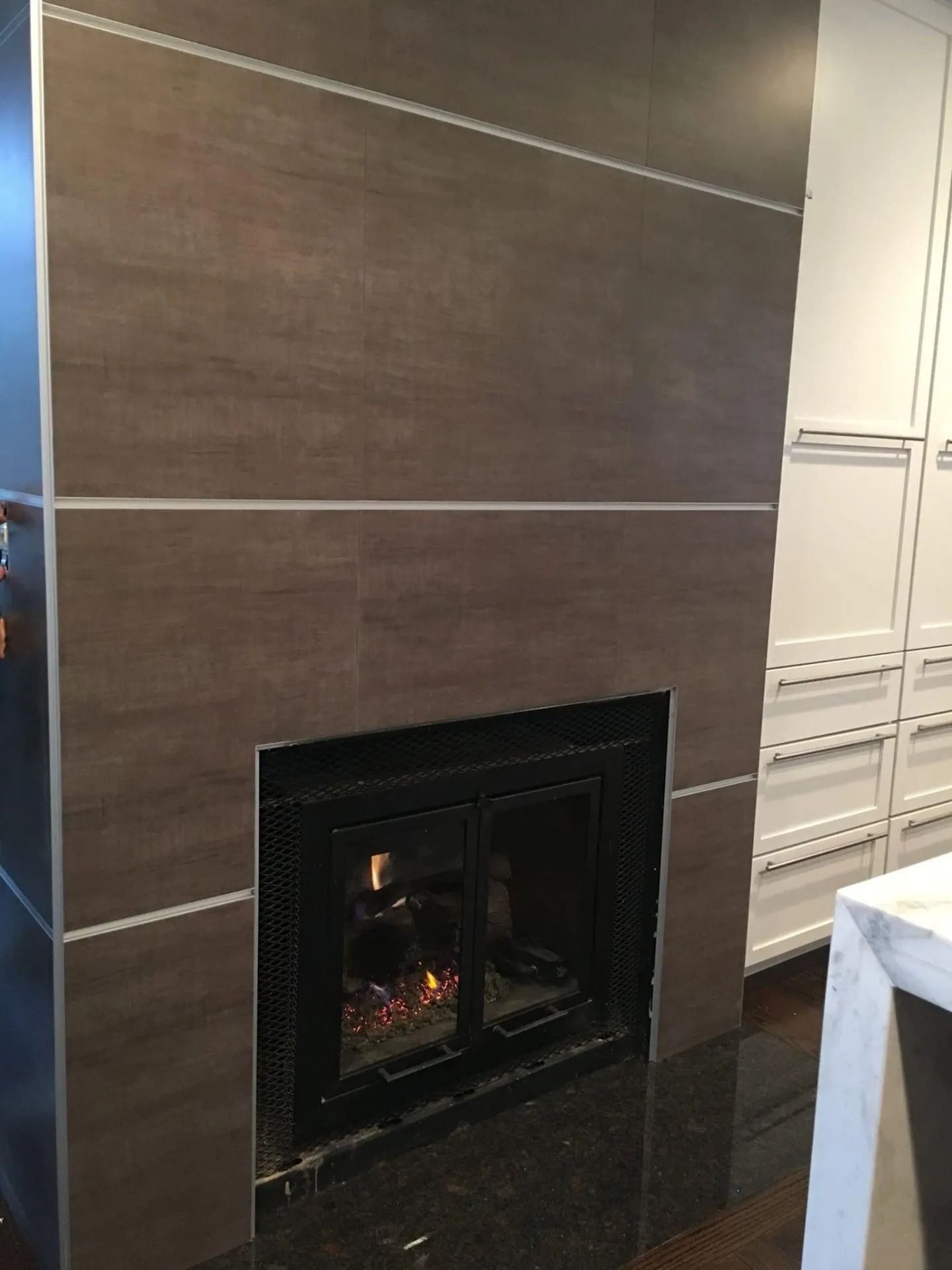 Brown tiled fireplace with a lit fire, surrounded by a black frame and granite hearth.
