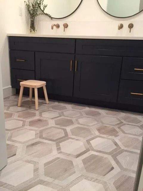 Bathroom with dark blue cabinets, gold fixtures, and light wood hexagon tiles. A small wooden stool is in front.