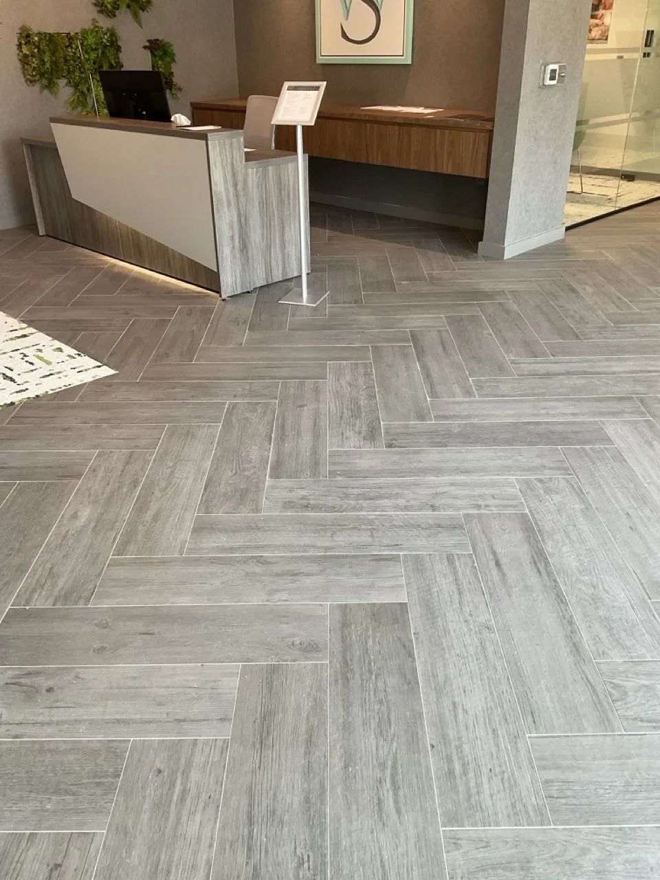 Reception area with gray herringbone-patterned floor, front desk, and a sign.