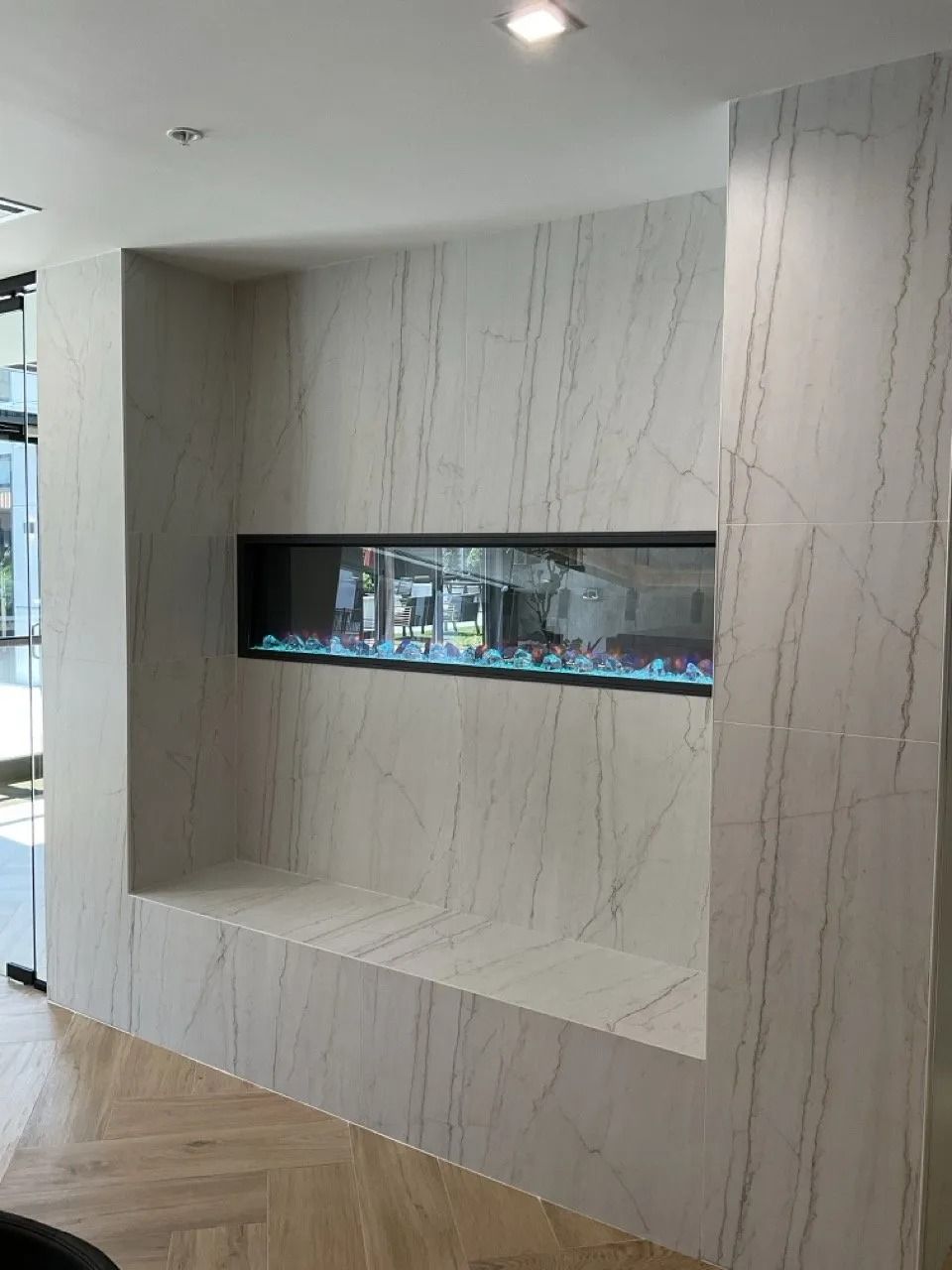 Modern fireplace built into a white marble wall with blue flames visible.
