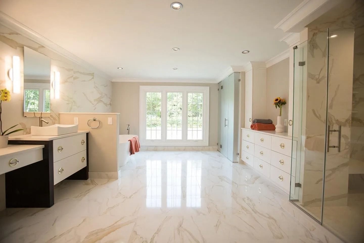 Spacious modern bathroom with marble floors, double vanity, glass shower, and doors to a backyard view.