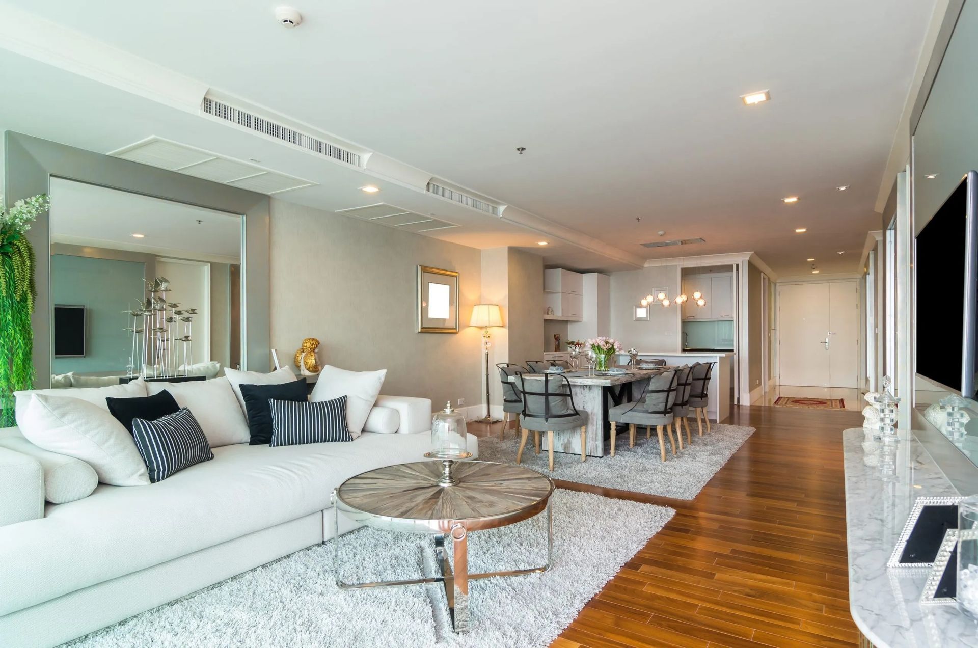 Bright, modern living room with white sectional, dining table, rug, and hardwood floor.