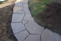 Stone pathway winding through a yard, bordered by dirt and grass.