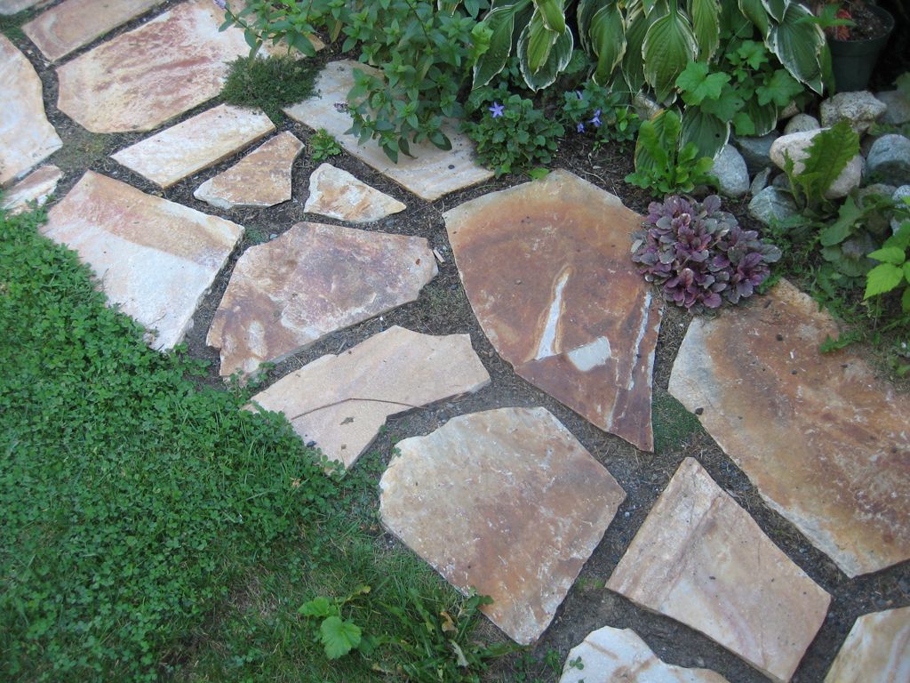 Stone pathway winding through a garden, bordered by grass and plants.