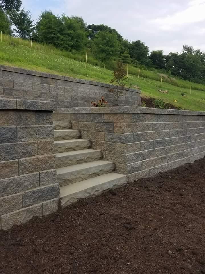 Stone retaining wall with built-in stairs leading up a grassy hillside.