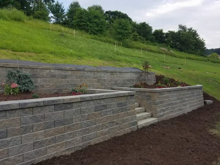 Stone retaining walls with steps and planted beds on a grassy hillside.