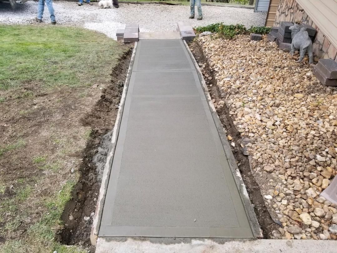 Newly poured concrete walkway with landscaping on either side.