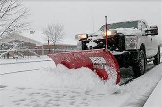 Snowplow clearing snow from a road in front of a building during a snowfall.