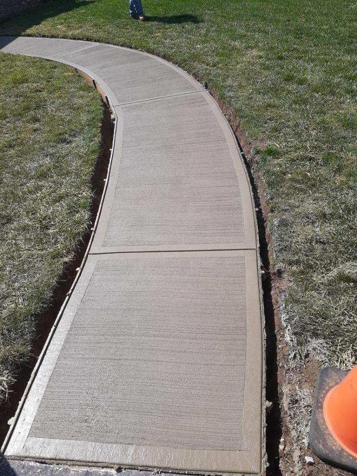Newly poured concrete sidewalk curving through a grassy yard.