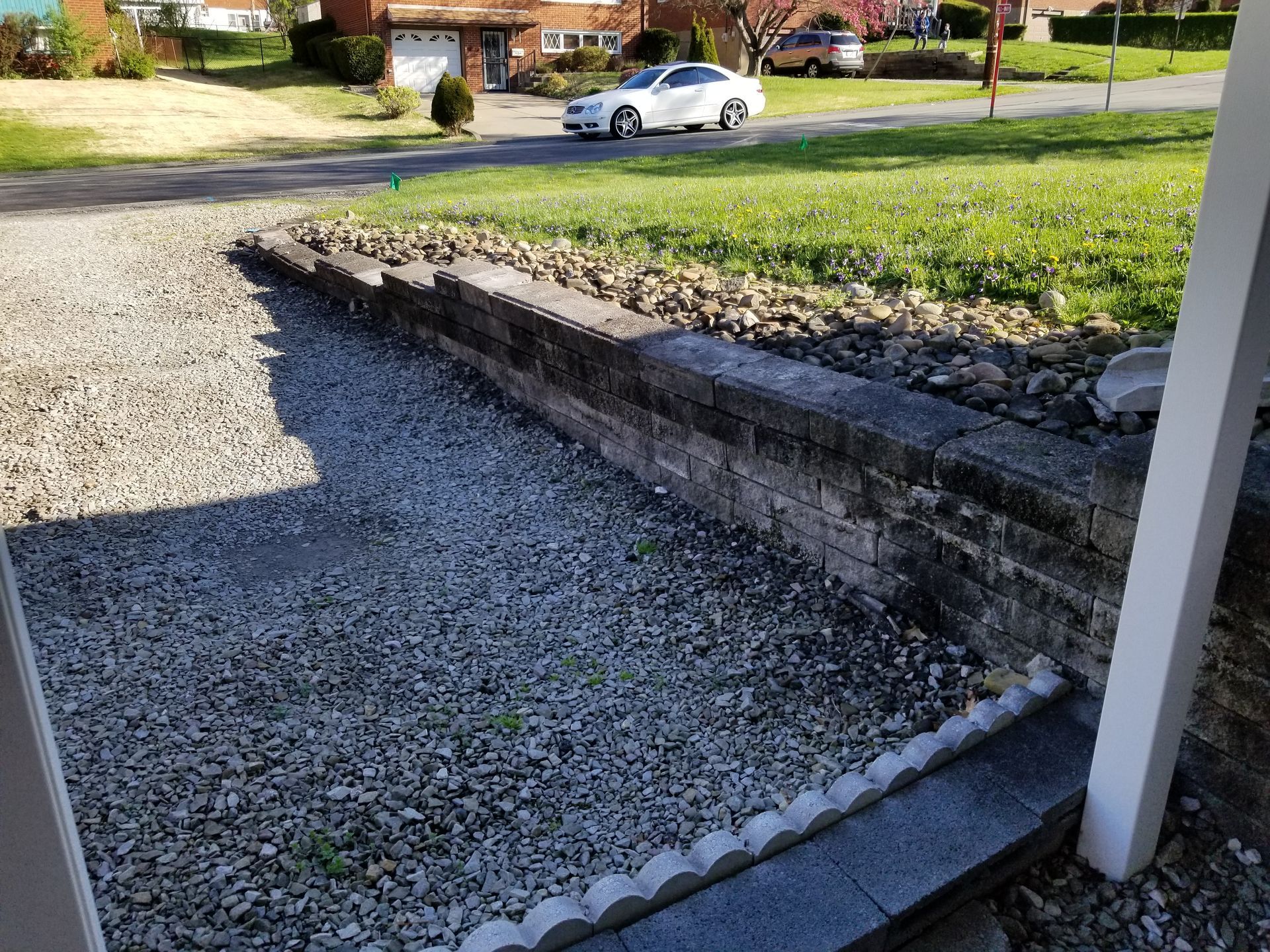 Gravel driveway leading to a house, bordered by a low stone wall, with a car approaching.