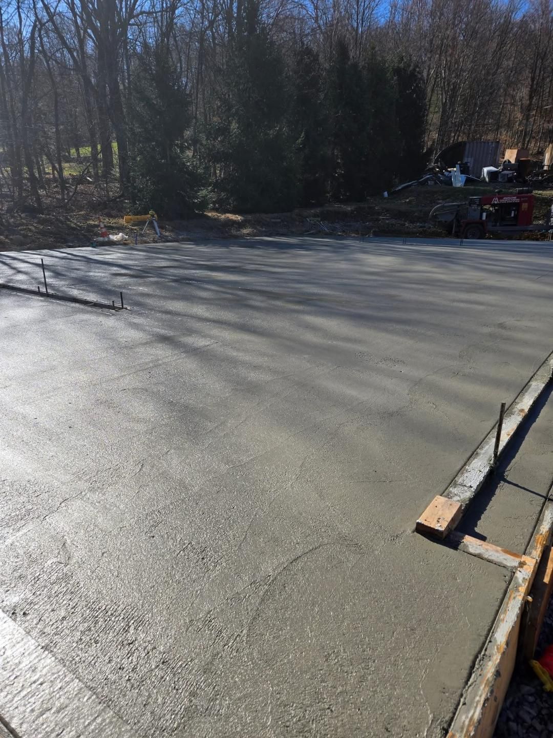 Freshly poured concrete slab, gray, smooth surface. Wood forms around the edges, forest background.