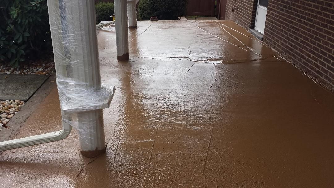 Brown-painted concrete porch with support columns. Cracks visible. Brick building in background.