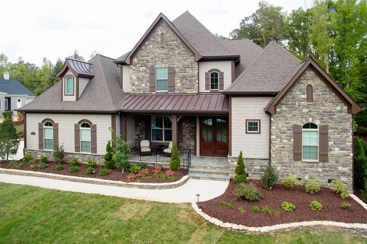 Large stone and beige house with brown roof and landscaping.