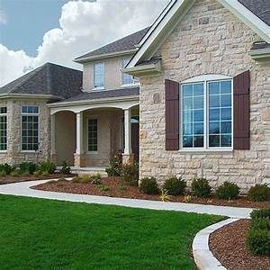 House with light-colored stone facade, brown shutters, and green lawn.