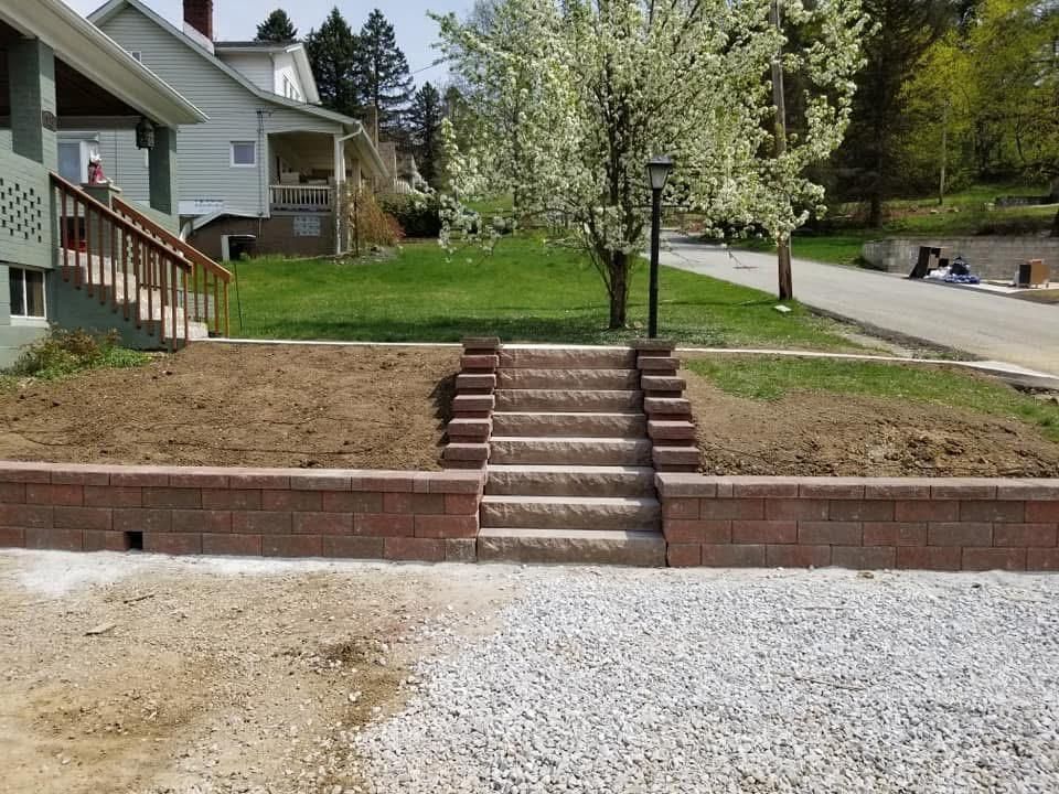 Brick retaining wall with steps leading up to a grassy yard. Brown soil on top of the wall.