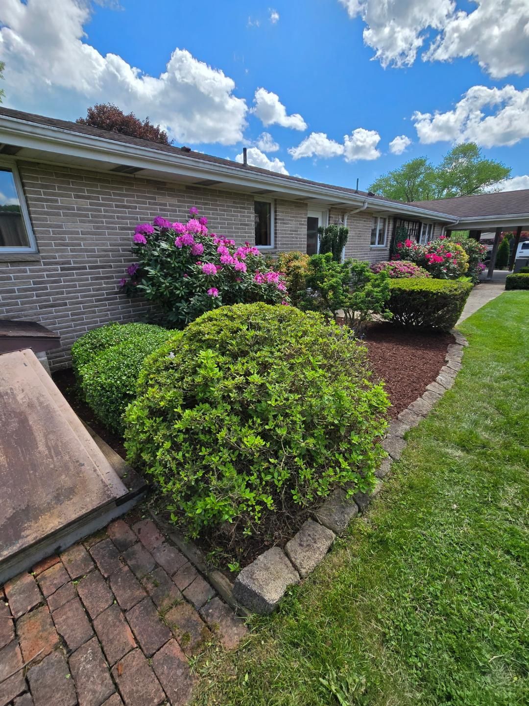 Brick house with colorful blooming bushes and a green lawn under a blue sky.