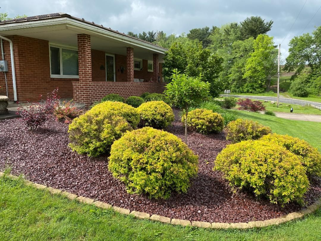 Brick house with porch and landscaped yard with rounded green shrubs on reddish-brown mulch.