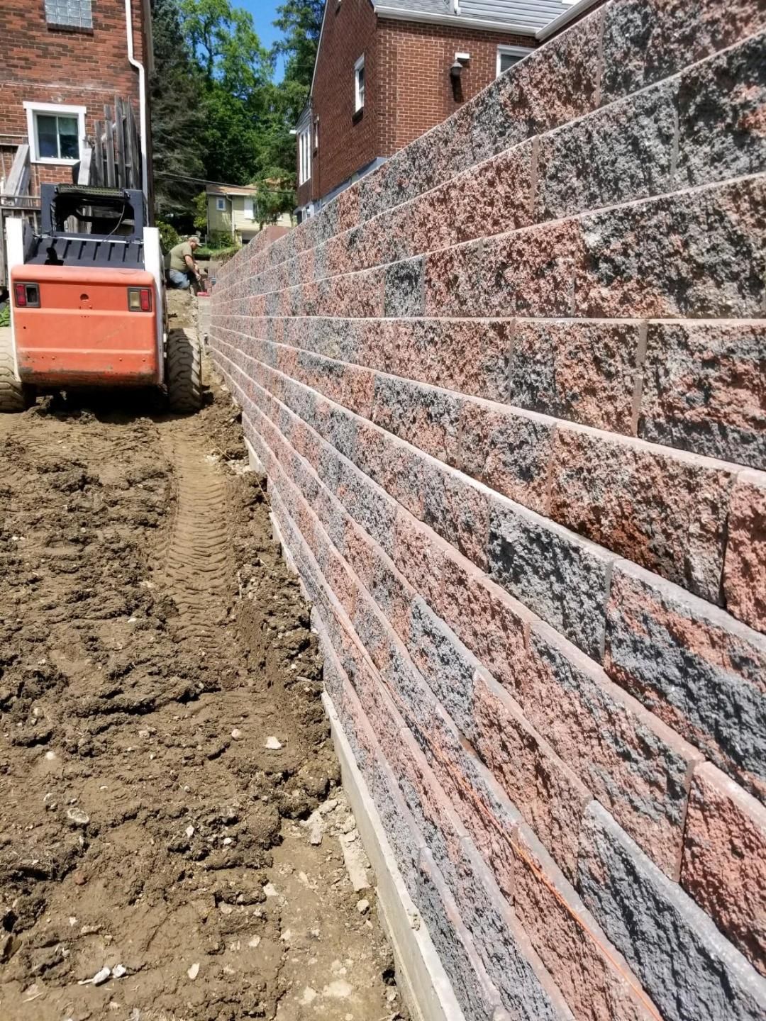 Orange construction equipment next to a retaining wall made of red and gray blocks.